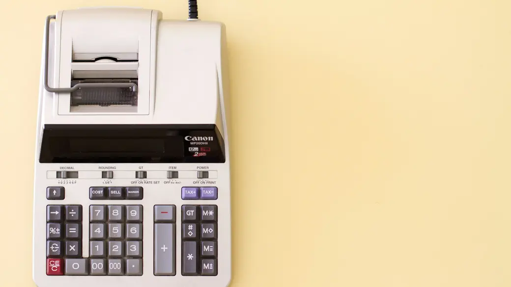 Calculadora e documentos de imposto ao lado de uma casa em miniatura